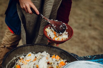Hand holding spoon for eating cooked rice with cooked pumpkin in a brown ceramic bowl