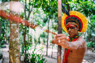 Indian from the Pataxó tribe using a bow and arrow. Brazilian Indian with feather headdress and...