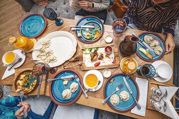A group of friends arranged a feast on the table in a restaurant with Georgian cuisine. Khinkali, tobacco chicken and wine in a clay jug