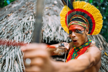 Indian from the Pataxó tribe using a bow and arrow. Brazilian Indian with feather headdress and...
