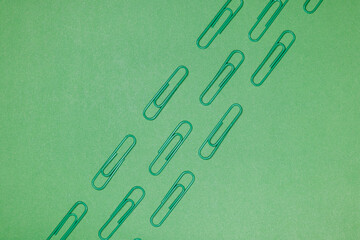 Green paper clips isolated on green background, close up, copy space. Top view. Back to school, college, education concept