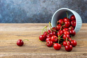 Ripe wet sweet cherries are poured out of the blue bowl on wooden