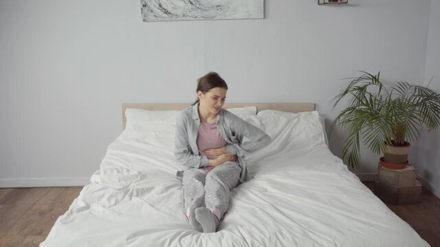 young woman suffering from stomach ache in bedroom
