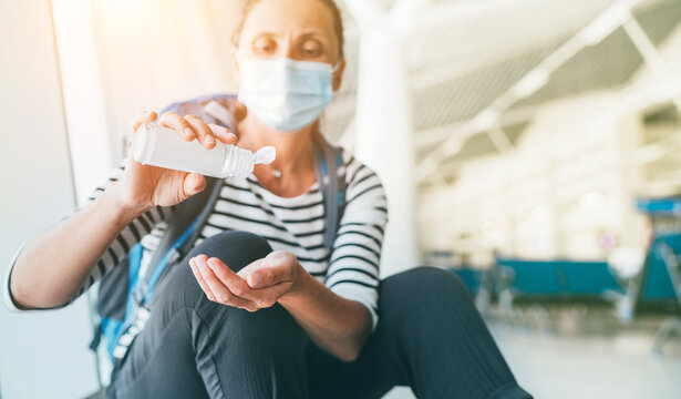 Female traveler with backpack sitting in airport passenger transfer hall in protective face mask applying Hand sanitizer gel. Personal hygiene and traveling in worldwide pandemic time concept image