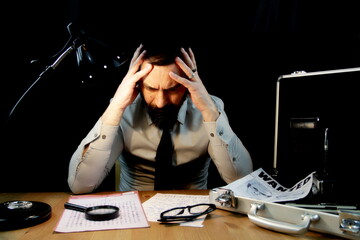 Detective sitting, tired, holding hands on head after examining documents of the Zodiac serial...