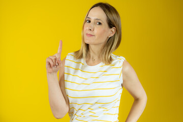 Portrait of beautiful young woman pointing up over yellow background.