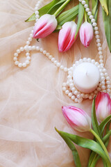 Fototapeta na wymiar romantic background with pink tulips, pearls and white candle on tulle fabric with space for text