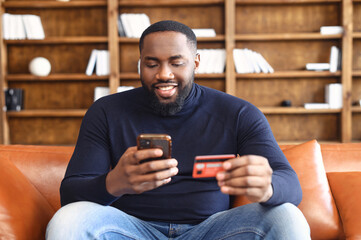 Online transaction, payment. African-american man holding credit card and using smartphone for...