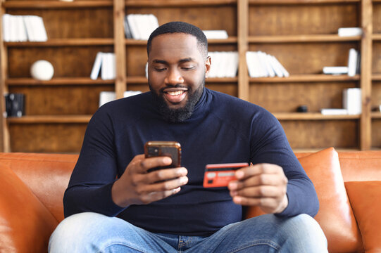 Online transaction, payment. African-american man holding credit card and using smartphone for shopping, a dark skinned guy with mobile phone and making purchases online