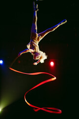 An aerial gymnast shows a performance with a ribbon in the circus arena.