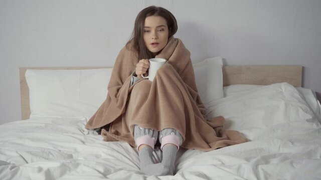 sick woman covered with blanket holding cup of tea