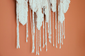 Macrame hangs on the brown wall. The fringe is white in close-up.