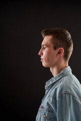 Portrait of a calm, serious young guy, a student, dressed in free-style clothes, standing on a black background in the studio. Transition age