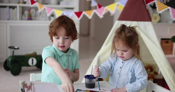 cute kids envolved in drawing activity with watercolor paints at cozy nursery room at home