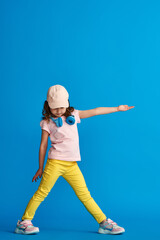 little girl in summer clothes and headphones poses on blue background in full growth and looks to side and points her hand to side. concept summer and spring casual children's clothing.