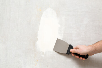 Young adult man hand using spatula and plastering wall with white fresh finishing putty. Closeup....