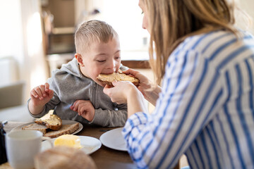 Single mother having breakfast with down syndrome child at home.