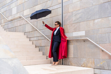 business woman dressed in red coat and suit holding an umbrella on modern design staircase on the street