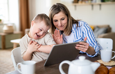 Single mother with down syndrome child at home, video call on tablet.
