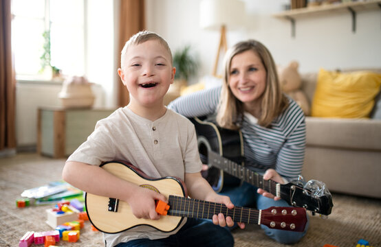 Single mother with down syndrome child at home, playing guitar.