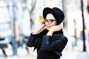 Beautiful russian girl dressed in black leather clothes and eyeglasses. Rock style european woman in urban background.