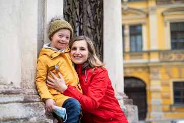 Single mother with down syndrome child outdoors in town, looking at camera.
