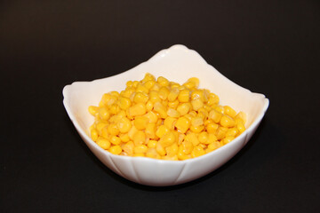 Canned sweet corn in white ceramic bowl isolated on black