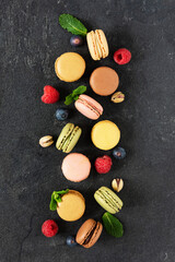 Multi colored french macaroons and berries such as raspberry and blueberry and mint leaves top view on black background.