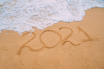 Closeup image of sea waves washing 2021 new year numbers from sand on the beach. Concept of New Year, Christmas and travel on winter holidays.