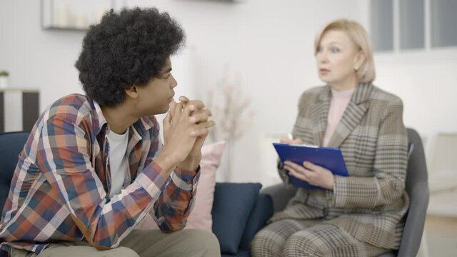 Depressed young man talking to teen therapist, addiction treatment, psychology
