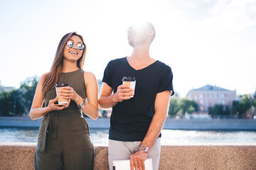 Backlit view of cheerful hipster guys with disposable takeaway cups enjoying friendly meeting...