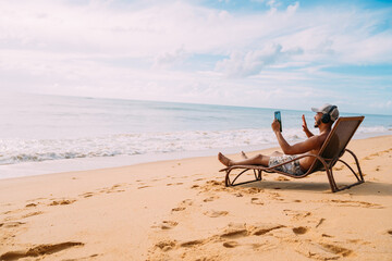 Man making a video call on summer vacation. latin american man sitting on the beach chair with...