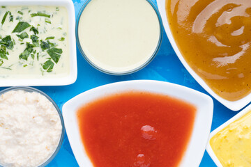 Different type of sauces in different white bowls on blue cement background