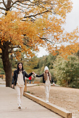 Fototapeta premium mom and daughter walk together in the autumn park by the hand