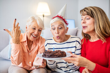 A beautiful senior lady making a wish and blowing candles on her lovely birthday cake. Birthday comes with many surprises. Happy mature woman celebrating birthday