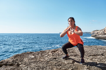 FITNESS WOMAN IN SPORTS SET TRAINING WITH ELASTIC BAND, WEIGHTS, GYM EXERCISES, IN FRONT OF THE WATER.