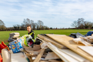 A young adult male builder wearing a high visibility vest throwing rubbish into a skip