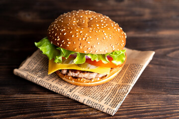 hamburger with cutlet, tomato and cheese on a dark wooden table and paper