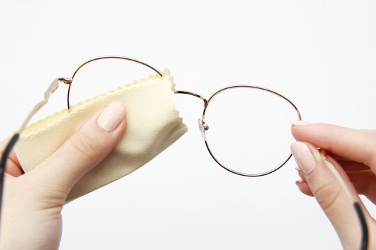 The girl manually cleans the lenses of her reading glasses on a light background. Soft cloth for wiping glasses and optics from dirt and dust. The concept of cleaning and caring for glasses.