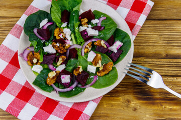 Tasty spinach salad with boiled beetroot, feta cheese, walnut and red onion on wooden table. Top view. Healthy vegetarian food