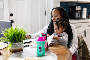 Black woman working from home with toddler child sitting on lap