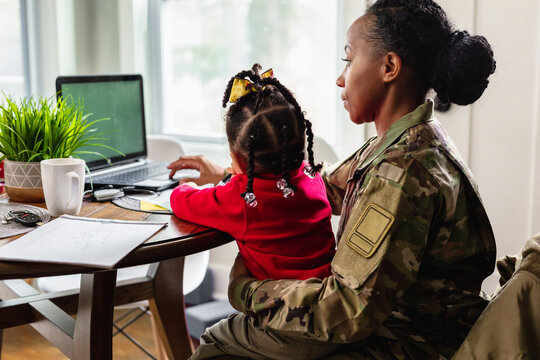 Focused military woman working from home at laptop with child