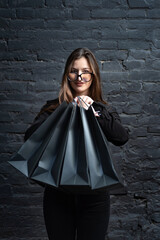 Naklejka premium Woman in black clothes holds black paper bags on dark background. Vertical frame