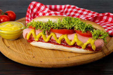 Hot dog with mustard, tomato and lettuce on wooden background
