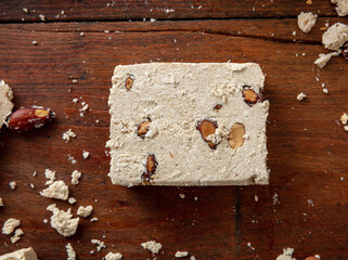 Halva slice with almonds on wooden table background, top view.