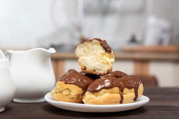 Eclairs drenched in chocolate with butter cream on white plate. Home made, kitchen on the background