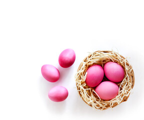 Wicker nest with pink colored eggs on white background