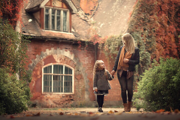Fototapeta na wymiar Beautiful blond mother and daughter are walking in gorgeous autumn park. Image with selective focus and toning