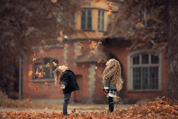 Beautiful long-haired blonde girl and a cute boy are throwing leaves up in autumn old park near the...