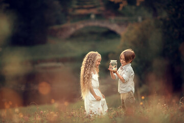 Beautiful long-haired girl and boy are looking at butterflies in the jar in summer park. Image with...